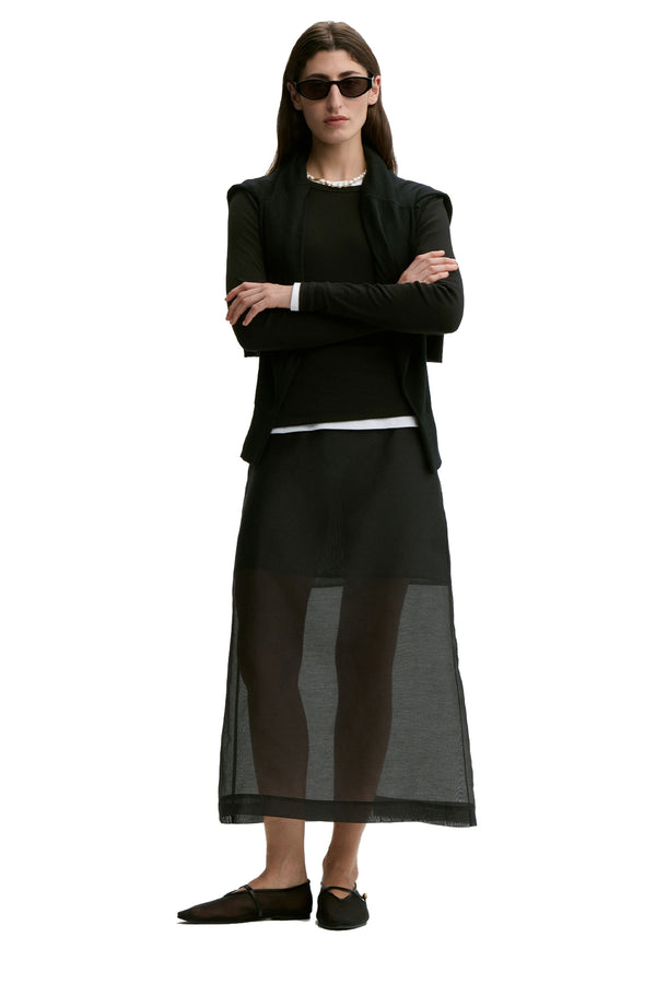 Front view of a woman wearing By Malene Birger translucent skirt in black, paired with black long sleeve top, black sunglasses and a pair of black flats, shown against a plain white background.