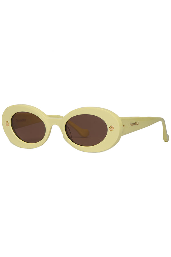 Rotated view of Nanushka oval sunglasses in pale yellow with metal moon signs, shown against a plaid white background.