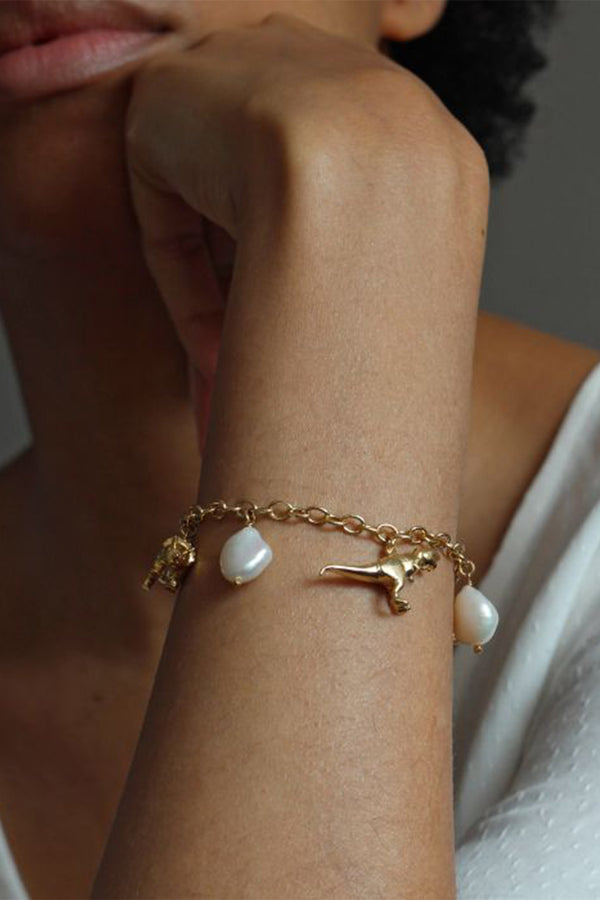 Model wearing the dinosaur and broque Pearl charm bracelet in gold and pearl colours from the brand ALEX MONROE