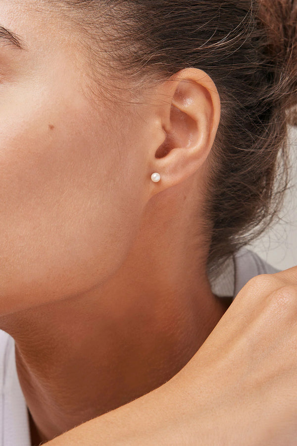 Model wearing the Coco stud earrings in gold and pearl colour from the brand ENAMEL COPENHAGEN