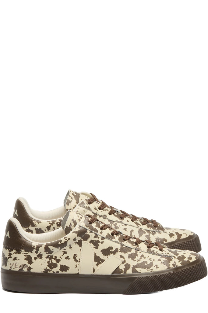 A pair of low-top sneakers featuring a brown and cream cow-print pattern, dark brown laces, and dark brown soles, shown against a plain white background.